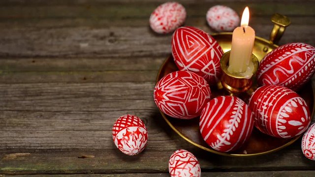 Closeup Red easter eggs with folk Ukrainian pattern lay around and on brass candlestick with burning candle on vintage boards background. Ukrainian traditional eggs pisanka and krashanka.