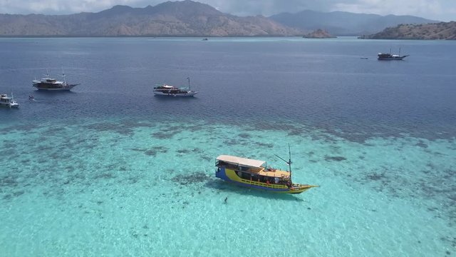 Aerial drone shot over some boats sailing through the sea in an idyllic seascape with an island in the background. Komodo Island, Indonesia.