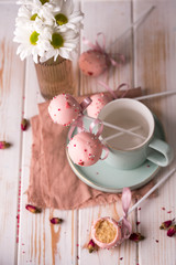 Composition cake pops with beautiful light utensils and in pink chocolate cream with powder on a wooden background.