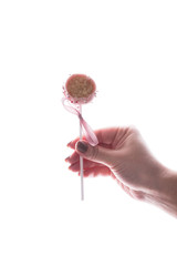 Cake pops in women's hands on a black background. Dessert in pink chocolate cream with powder and bow.