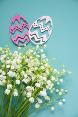 Floral blue background with fresh flowers. Spring greeting card for Easter. A bouquet of lily of the valley and a gift, eggs
