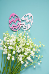 Floral blue background with fresh flowers. Spring greeting card for Easter. A bouquet of lily of the valley and a gift, eggs