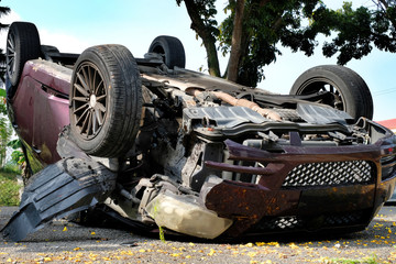 An overturn car lying upside down on a street after an accident, suffering heavy damage. Car lands...