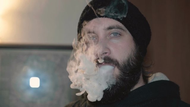 View of young man vaping with electronic cigarette and make smoke clouds