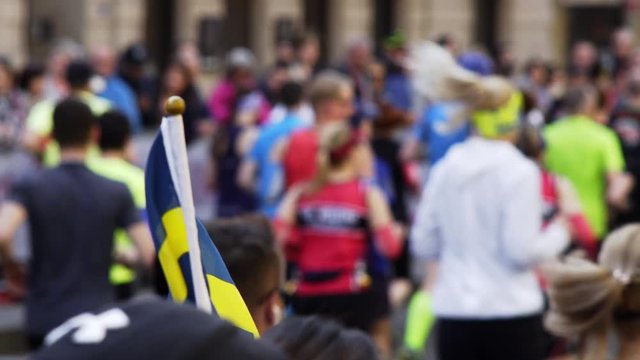 Defocused international half marathon participants run fast along wide Prague street and Sweden flags wave on foreground 