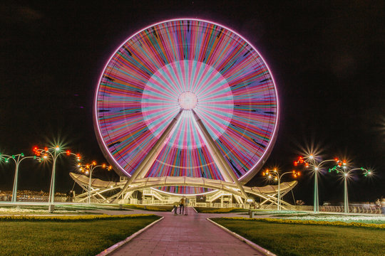 A colourful ferris wheel at night. Front view. Big carousel in Baku. Night fun. Ferris wheel against a dark sky background. Ferris wheel and rollercoaster in motion. Long exposure light image