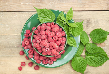 Raspberry in a bowl with fresh leaves and  berries scattered around on wooden table on rustic background, closeup, copy space, healthy vegan eating and organic homegrown food concept