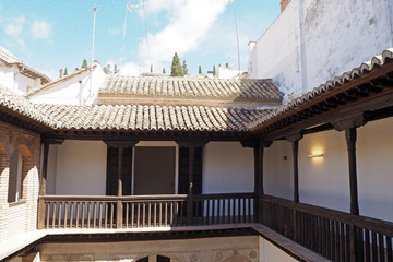 The part of the medieval stone Arabic house with columns, the balcony with the wooden decorative wall, the tiled roof.