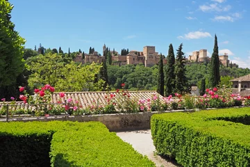 Washable wall murals Khaki The landscape with the green garden decorative plants and pink blooming flowers, the red tiled roof, the medieval stone fortress. It is the sunny day in the old European town.