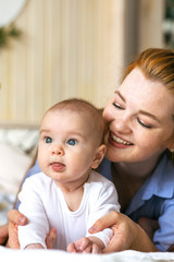 A young mother hugs and caresses a three-month-old baby in bed. Moments of happy motherhood