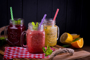 three Freshly blended fruit smoothie in glass jar with straw on a dark wood background, Healthy fruit and vegetable smoothies, detox berry drinks, Healthy food for breakfast and snack