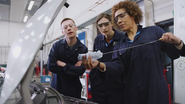 Female tutor with students checking oil level in car engine on auto mechanic course at college - shot in slow motion