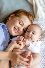 A young mother hugs and caresses a three-month-old baby in bed. Moments of happy motherhood