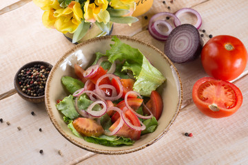 Fresh salad with greens, vegetables, onions and pepper stands on the table in the restaurant