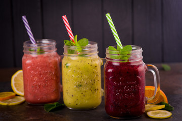 Fototapeta na wymiar three Freshly blended fruit smoothie in glass jar with straw on a dark wood background, Healthy fruit and vegetable smoothies, detox berry drinks, Healthy food for breakfast and snack