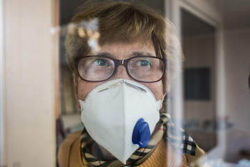 Seniorin mit Mundschutz schaut aus dem Fenster