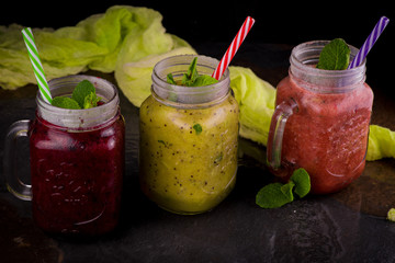 three Freshly blended fruit smoothie in glass jar with straw on a dark wood background, Healthy fruit and vegetable smoothies, detox berry drinks, Healthy food for breakfast and snack