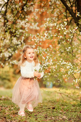 Obraz na płótnie Canvas A beautiful cute little girl laughs and has fun in a flying nude skirt and a white fur blouse with a bouquet of blossoming cherry flowers in a spring botanical garden. For Easter and spring cards
