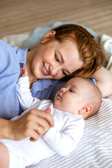 A young mother hugs and caresses a three-month-old baby in bed. Moments of happy motherhood