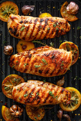 Grilled chicken breasts with thyme, garlic and lemon slices on a grill pan, top view