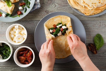 Pancakes with spinach, feta and dried tomatoes. Served on a gray plate. Wooden natural background.