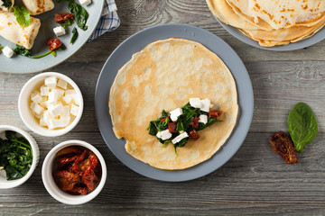 Pancakes with spinach, feta and dried tomatoes. Served on a gray plate. Wooden natural background.