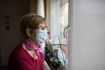 Seniorin mit Mundschutz schaut aus dem Fenster