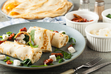 Pancakes with spinach, feta and dried tomatoes. Served on a gray plate. Wooden natural background.