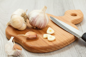 Ripe garlic heads and stainless steel knife on wooden cutting board