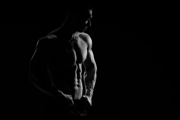 Muscular model sports young man in jeans showing his press on a black background. Fashion portrait of sporty healthy strong muscle guy. Sexy torso.  Black and white photography
