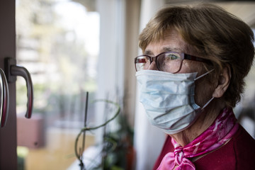 Seniorin mit Mundschutz schaut aus dem Fenster