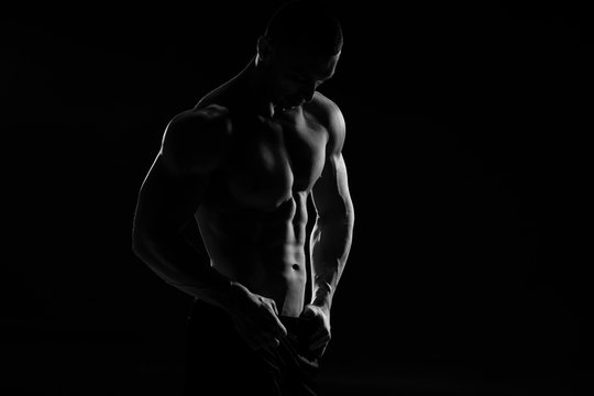 Muscular model sports young man in jeans showing his press on a black background. Fashion portrait of sporty healthy strong muscle guy. Sexy torso.  Black and white photography
