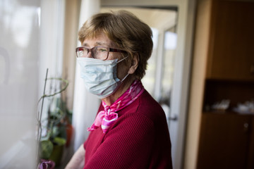 Seniorin mit Mundschutz schaut aus dem Fenster