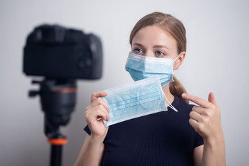 Young caucasian girl woman wearing mask, making a video blog (vlog) with camera at home
