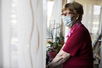 Seniorin mit Mundschutz schaut aus dem Fenster