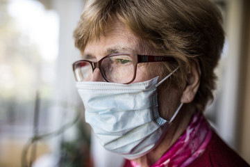 Seniorin mit Mundschutz schaut aus dem Fenster