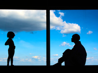 Silhouettes of Mom with a daughter of 3 years in front of a large window with blue sky and clouds. Stay at home for the quarantine prevention of the coronavirus pandemic. Self-isolation