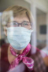 Seniorin mit Mundschutz schaut aus dem Fenster