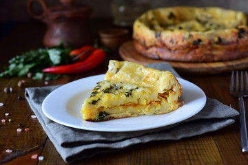A piece of cabbage pie on a white plate in the foreground, cabbage pie on a wooden platter in the background