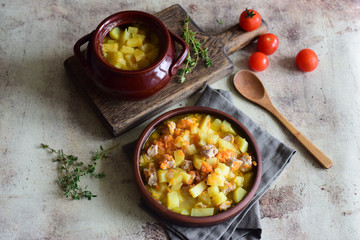 A hearty lunch: potatoes with meat baked in clay pots. Hot roast of potatoes and pork in a beautiful clay plate on a gray background