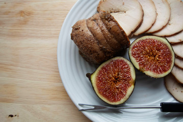 On a white plate meat roll with chopped ripe figs. The roll is cut into round pieces