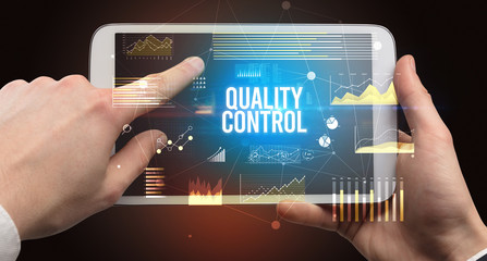 Close-up of hands holding tablet with QUALITY CONTROL inscription, modern business concept