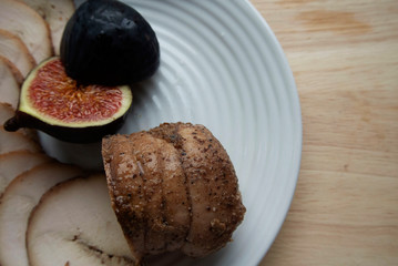 On a white plate meat roll with chopped ripe figs. The roll is cut into round pieces
