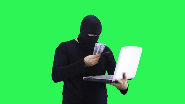 A man in a black mask agrees on a laptop showing money, on a green background