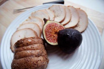 On a white plate meat roll with chopped ripe figs. The roll is cut into round pieces