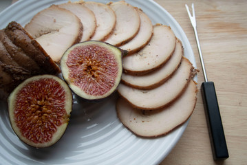On a white plate meat roll with chopped ripe figs. The roll is cut into round pieces