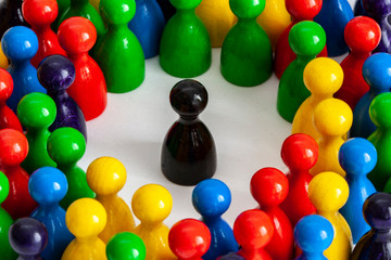 Black game figurine among a group of many figurines, symbolizing concept of being singled out,...