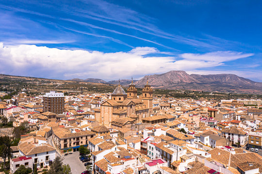 Aerial Drone photo of a beautiful city in a Almeria, Andalucia, Spain called Velez Rubio with red and orange house roof tops and a beautiful cathedral in the heart of the town with blue sky & mountain