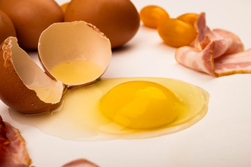 Broken chicken egg, chicken eggs, bacon slices and tomatoes on a white background. Close up.