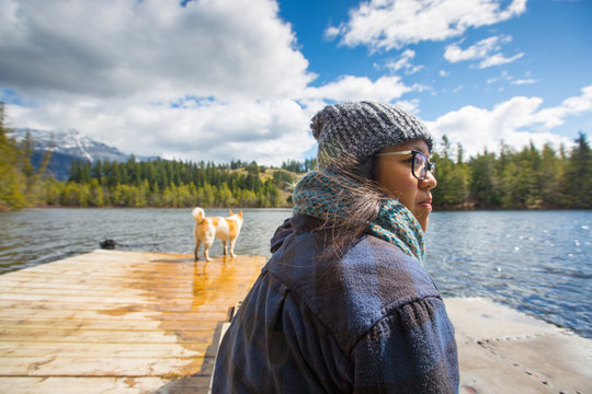 Woman sitting on a dock with her dog a lake below Curry peak in Pemberton, British Columbia, Canada.